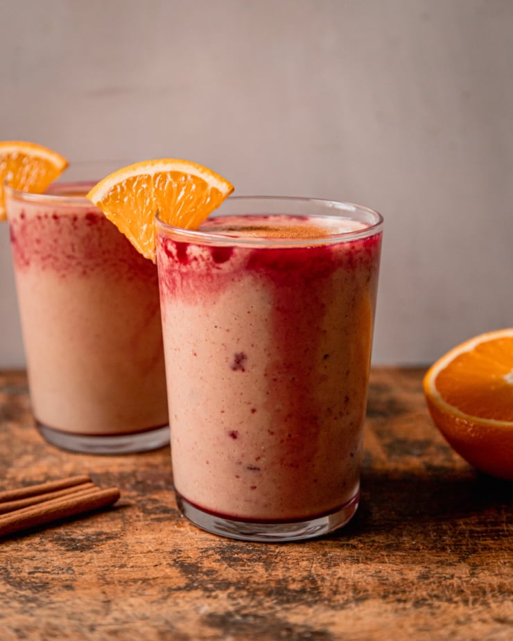 A head-on shot shows two glasses filled with an orange cranberry smoothie mixture. the glasses are garnished with little orange slices on the rims.