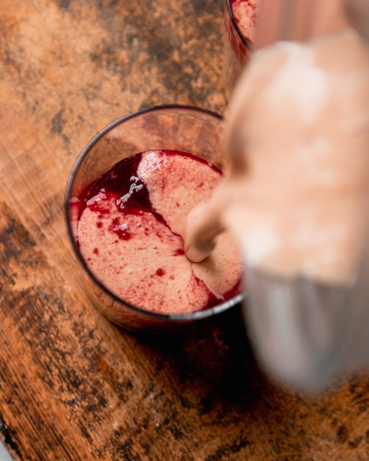 An overhead shot shows a smoothie being poured into a glass that had a bit of cranberry juice in the bottom. The result is tie dye-like stripes.