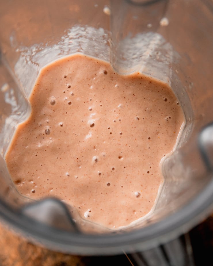 An up close, overhead shot shows a freshly blended orange cranberry smoothie in a blender jar.