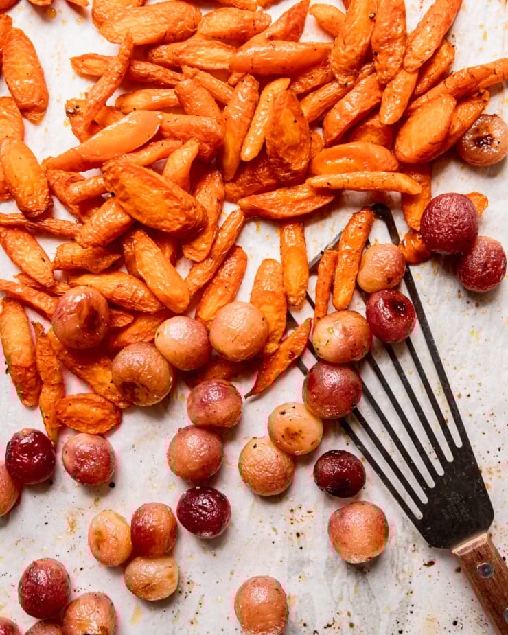 An overhead shot shows cooked carrots and caramelized grapes on a parchment-lined baking sheet.