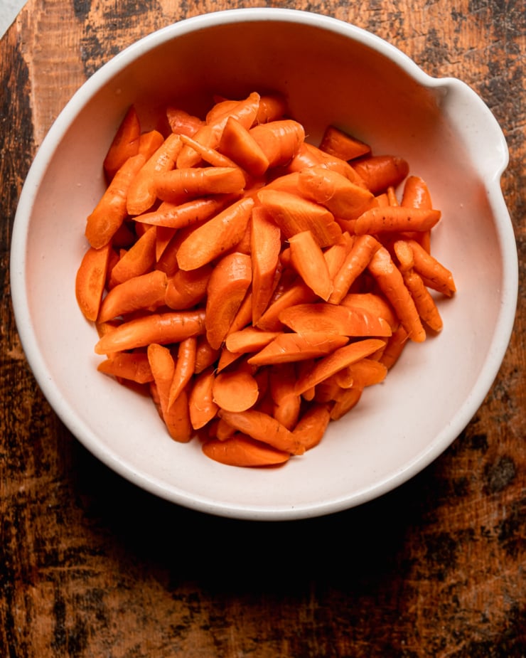 An overhead shot shows chopped carrots in a large, beige mixing bowl.