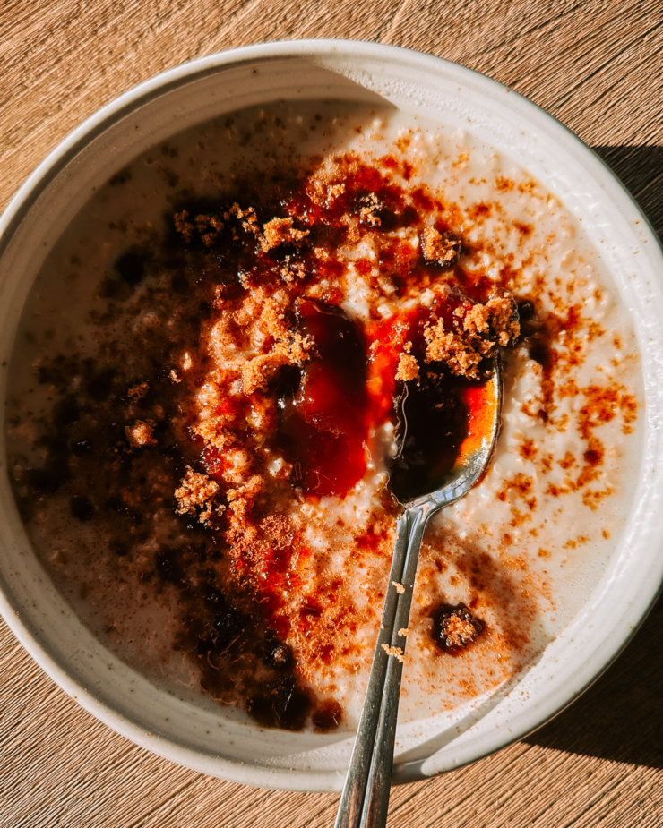 An overhead shot shows a bowl of steel cut oat porridge with a spoonful of apple butter and brown sugar sprinkled over the top.