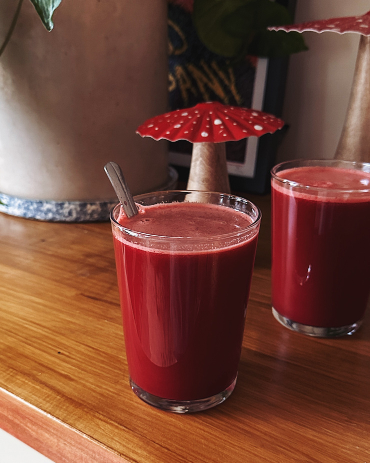 A head-on shot shows two glasses of a fresh fuschia-toned juice with beets, grapefruit, apple, cucumber, carrot, lemon, and ginger.