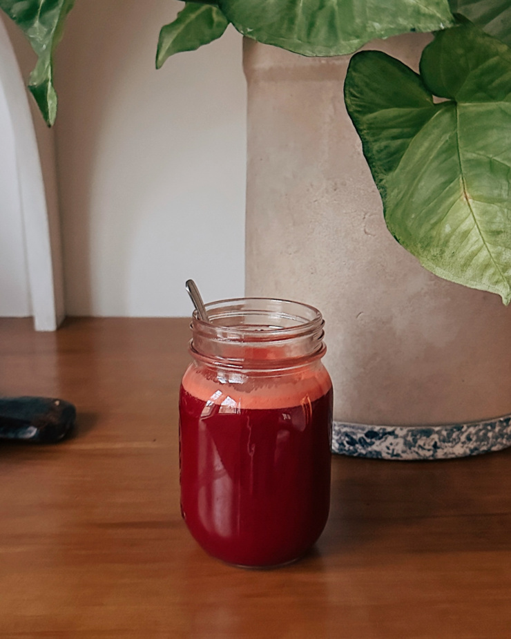 A head-on shot of a mason jar of deep burgundy juice on a wood countertop.