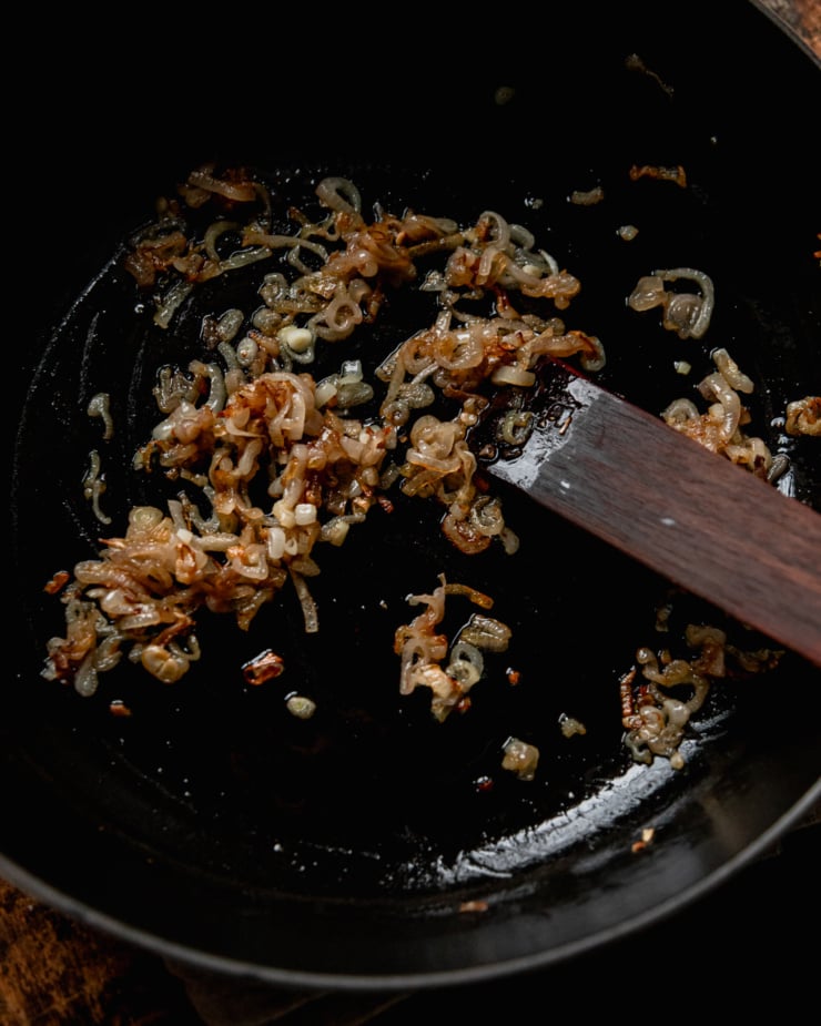 An overhead shot shows caramelized shallots in a pan with a wooden cooking utensil.