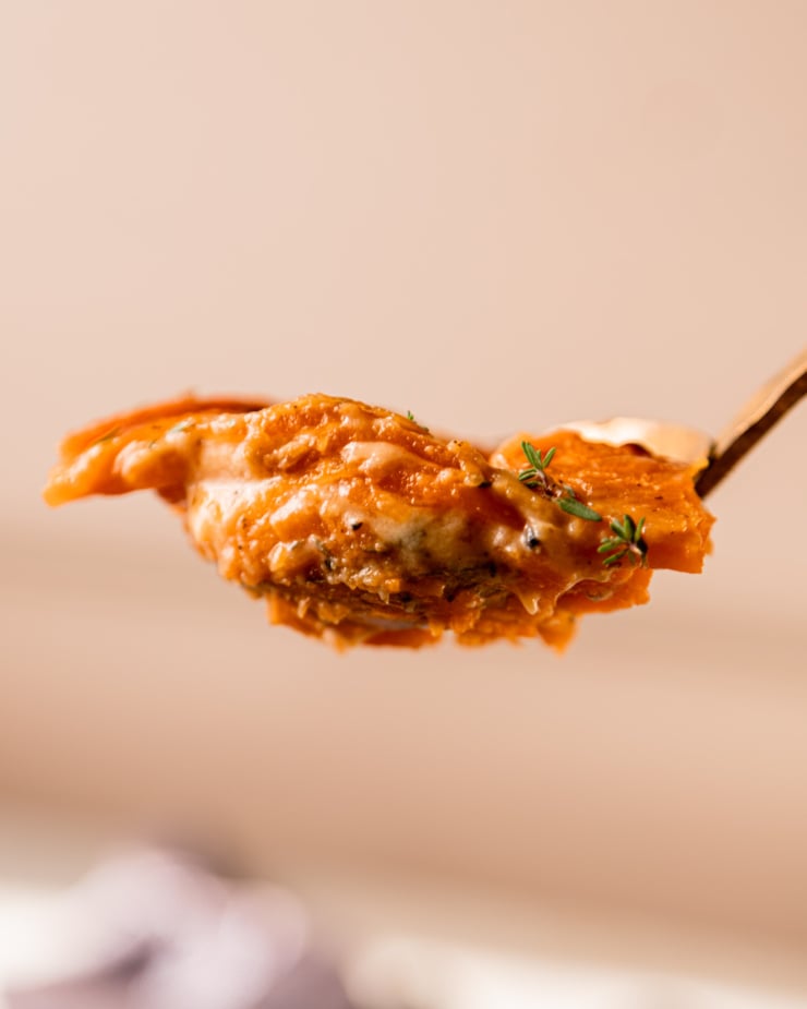 An up close shot shows a spoonful of gooey vegan sweet potato gratin with a few thyme leaves on top.
