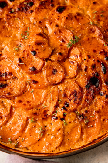 An up close, overhead shot shows a vegan sweet potato gratin in a ceramic baking dish. The top is broiled and browned in spots.