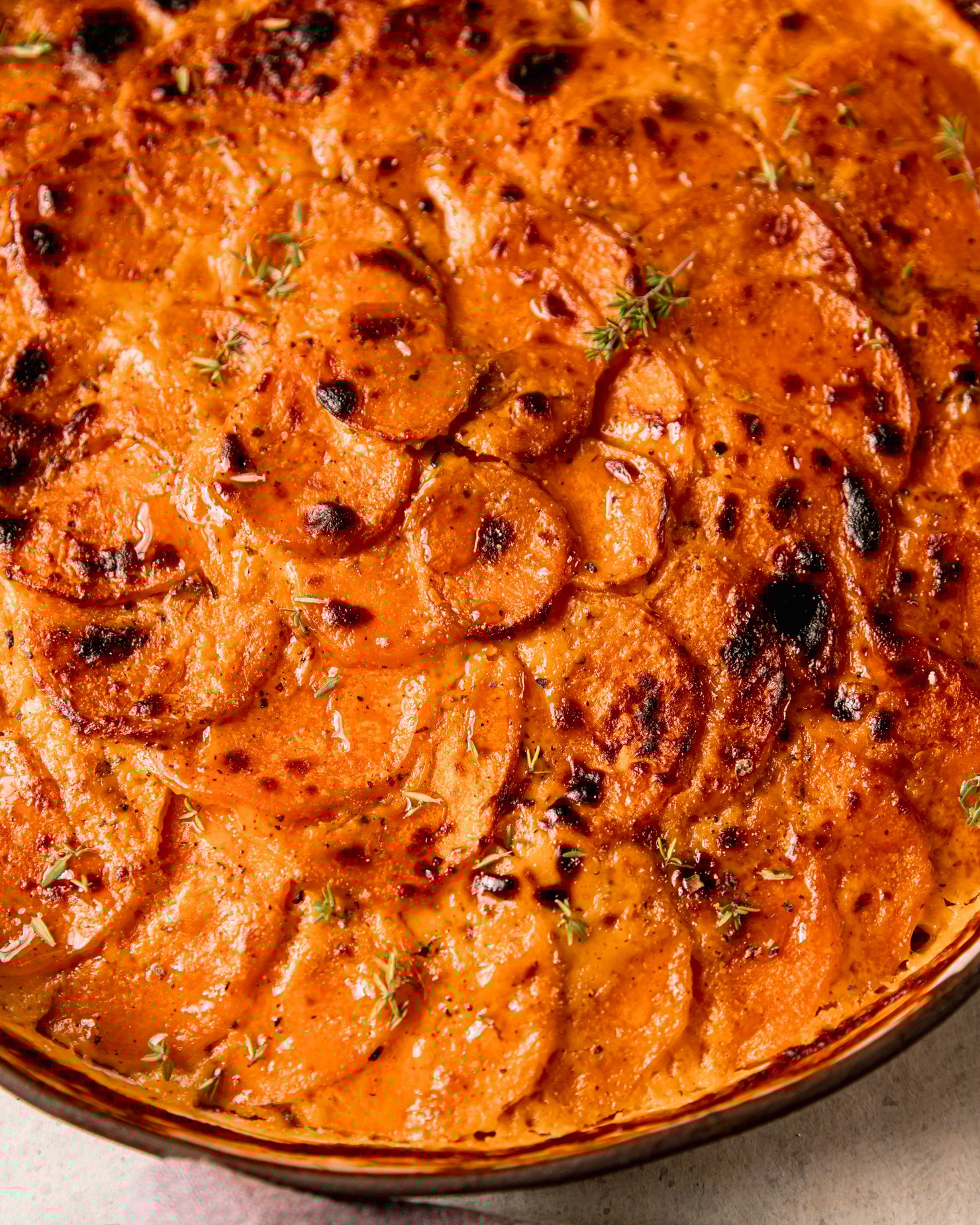An up close, overhead shot shows a vegan sweet potato gratin in a ceramic baking dish. The top is broiled and browned in spots.