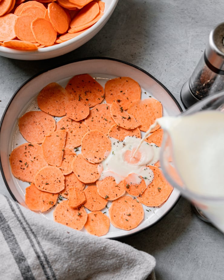 An overhead shot shows cashew "cream" being poured on top of sweet potato slices in a ceramic baking dish.