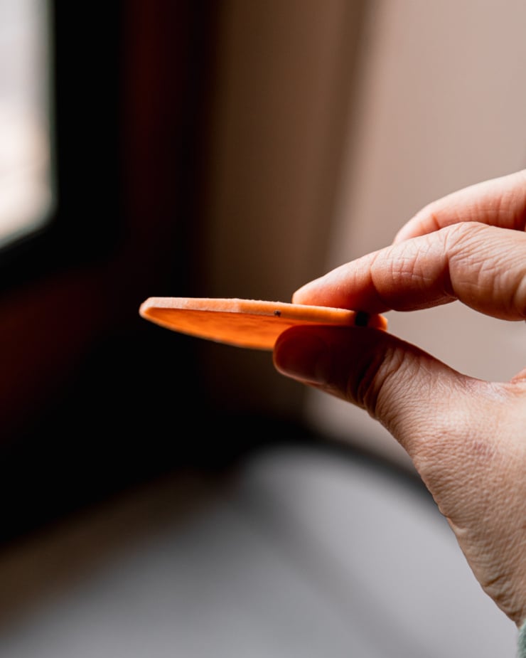 An up close shot shows a hand holding a thin slice of sweet potato to show the thickness--about 1/8 of an inch.