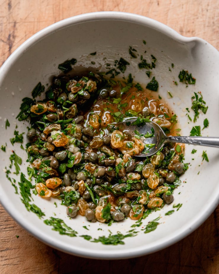 An overhead shot shows a bowl with caper raisin relish and a spoon sticking out.