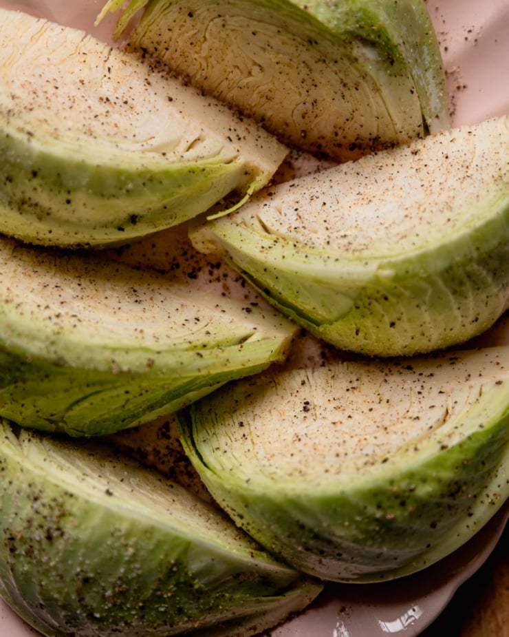 An up close, overhead shot shows wedges of cabbage heavily seasoned with salt and pepper.
