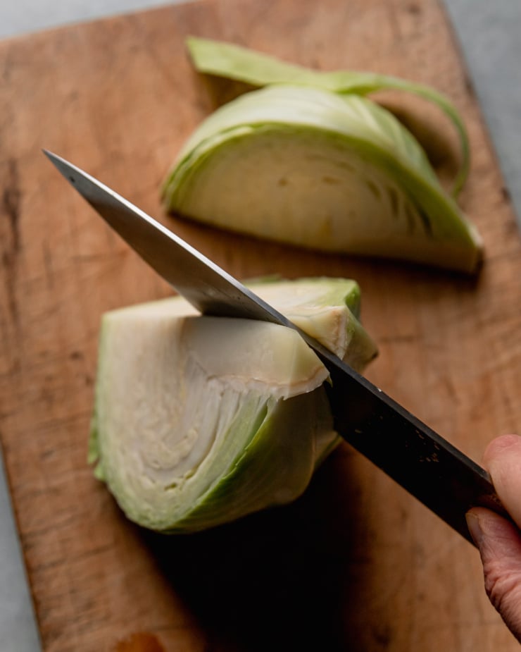 A 3/4 angle shot shows a knife cutting through the core of half a cabbage, making wedges.