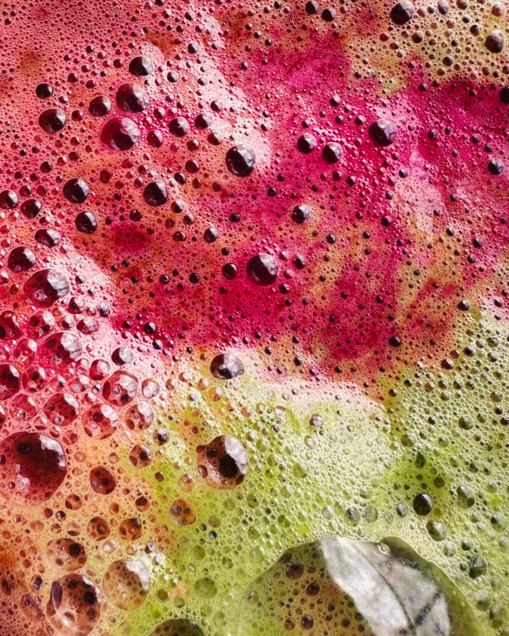 An up close, overhead shot shows fuchsia and green juice foam.