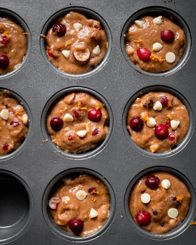 An overhead shot shows raw cranberry clementine muffin batter in muffin tin cups.