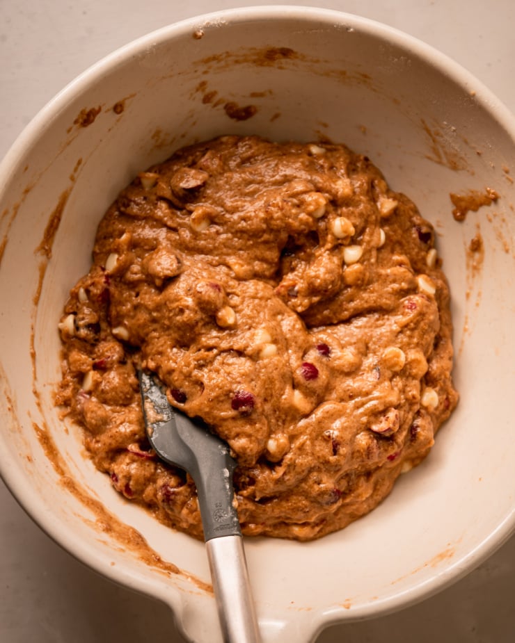 An overhead shot shows freshly mixed cranberry clementine muffin batter in a mixing bowl with a spatula sticking out.