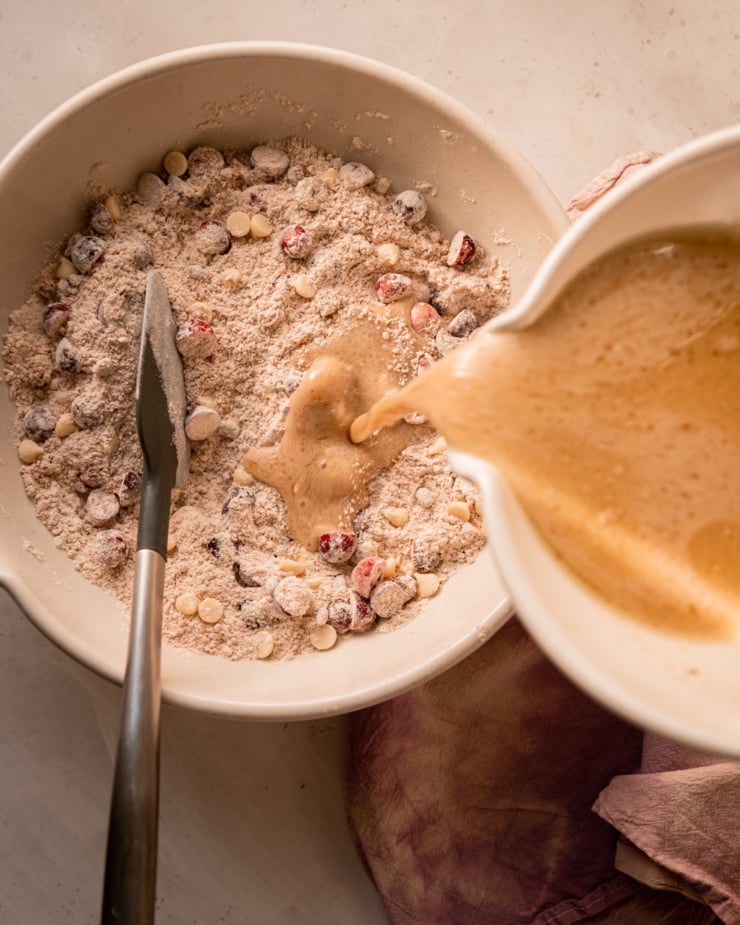 An overhead shot shows wet ingredients being poured into a large bowl with dry ingredients.