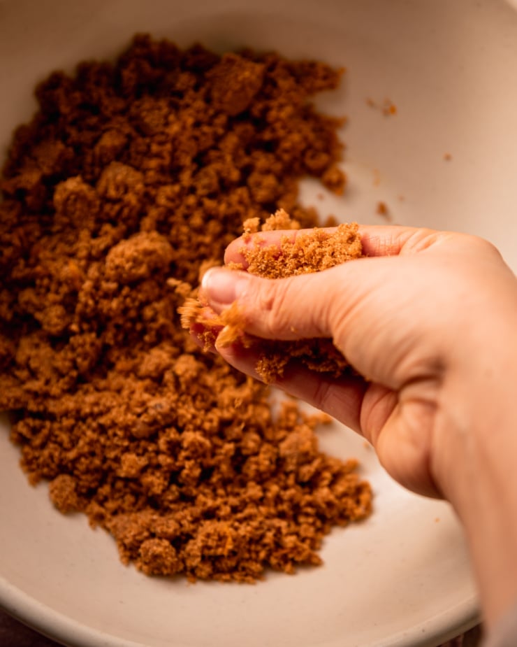 An overhead shot shows a hand working clementine zest into some brown sugar.