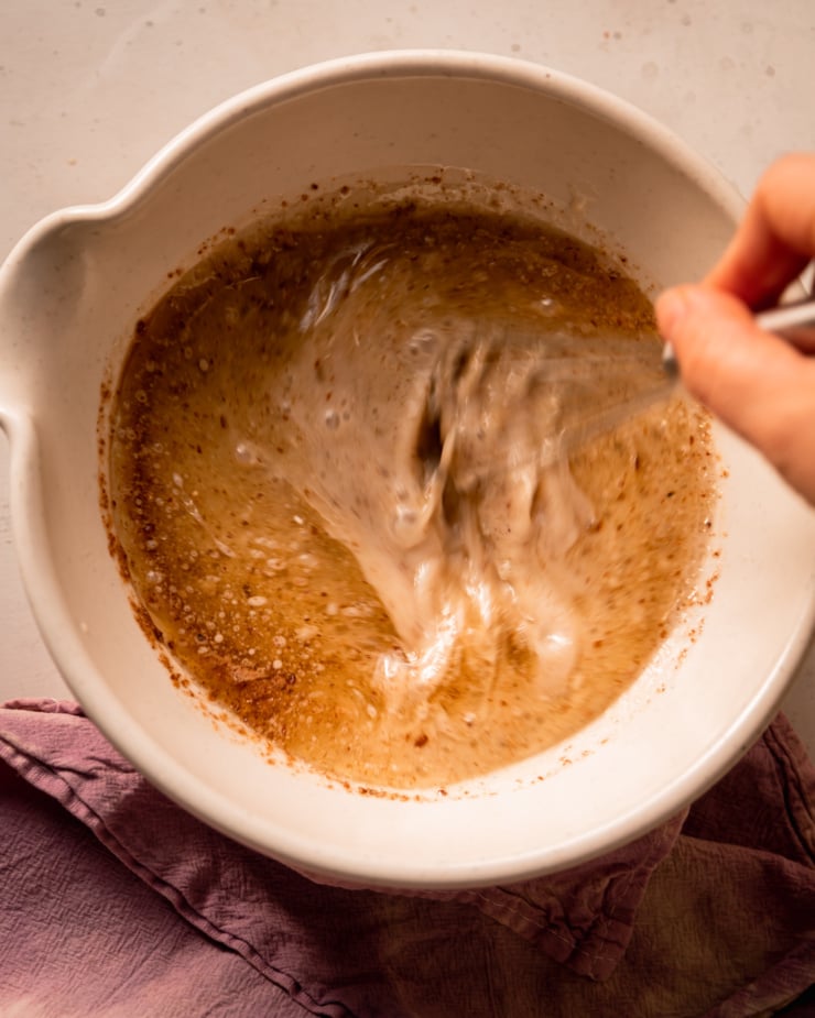 An overhead shot shows a hand using a whisk to bring liquid ingredients together in a bowl.
