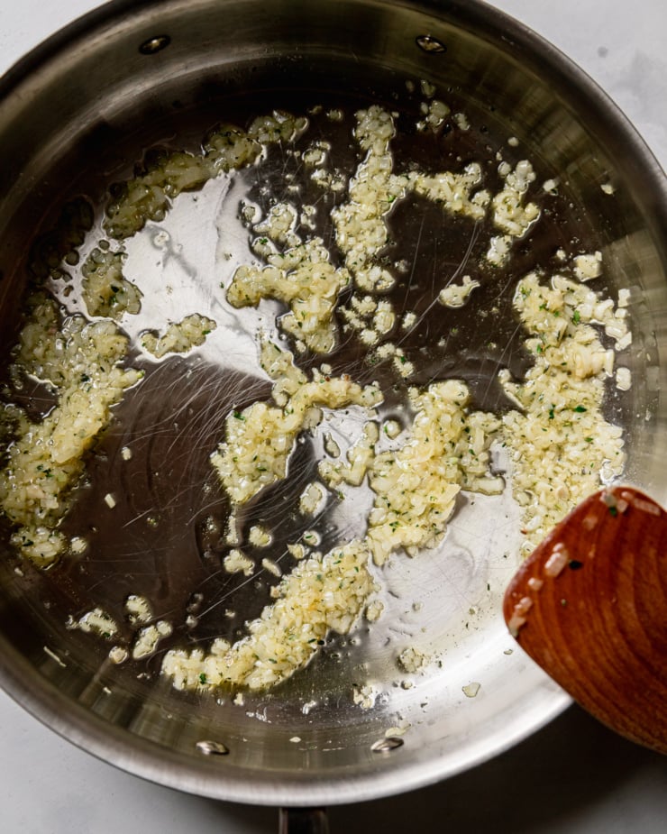 An overhead shot shows finely minced shallots and thyme sautรฉing in olive oil in a stainless steel skillet.