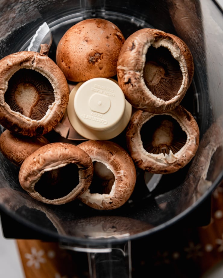 An overhead shot shows cremini mushroom caps in th ebowl of a food processor.