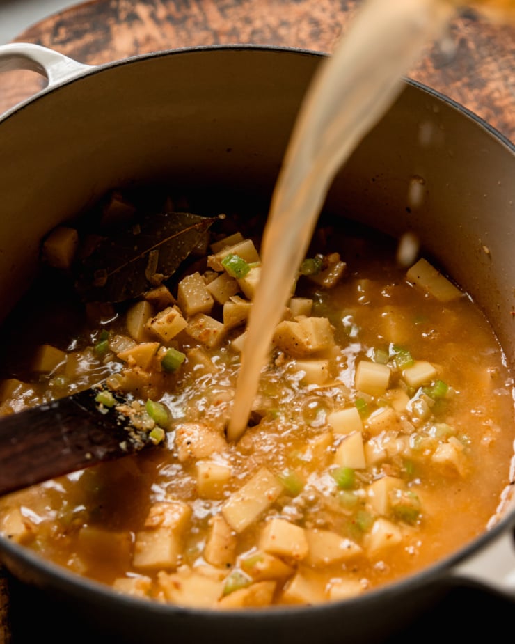 A 3/4 angle shot shows vegetable stock being poured into a pot for some soup.