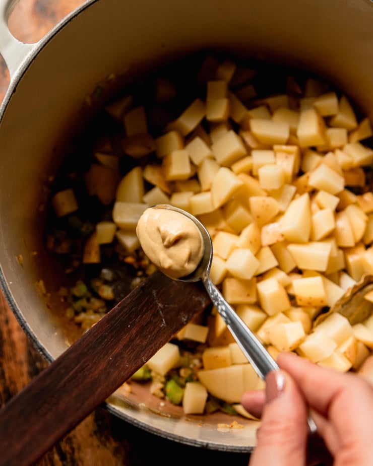 AN overhead shot shows Dijon mustard being added to a pot with sautéed vegetables.