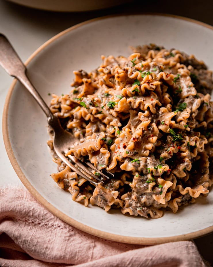 A 3/4 angle shot shows a bowl of creamy vegan pasta with a finely chopped mushroom and miso sauce. The pasta shape is like little ruffles and the whole dish is garnished with parsley.