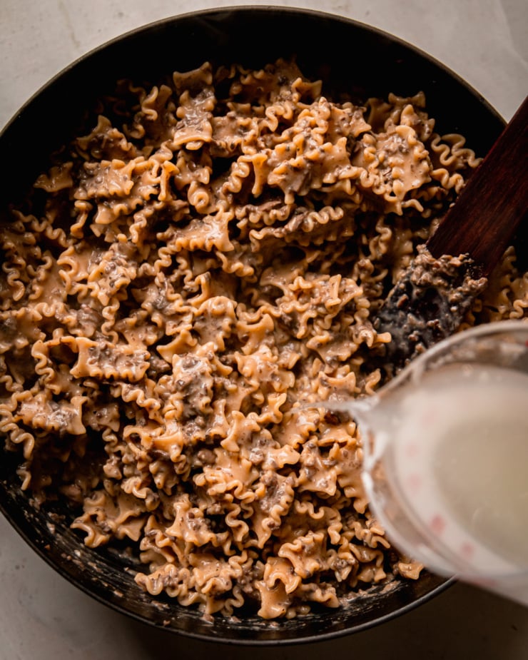An overhead shot shows starchy pasta water being poured into a braiser pot filled with pasta.