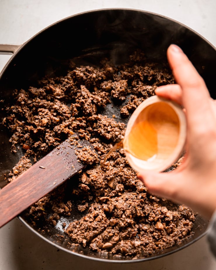 An overhead shot shows sherry vinegar being poured into a pot with mushroom duxelles.