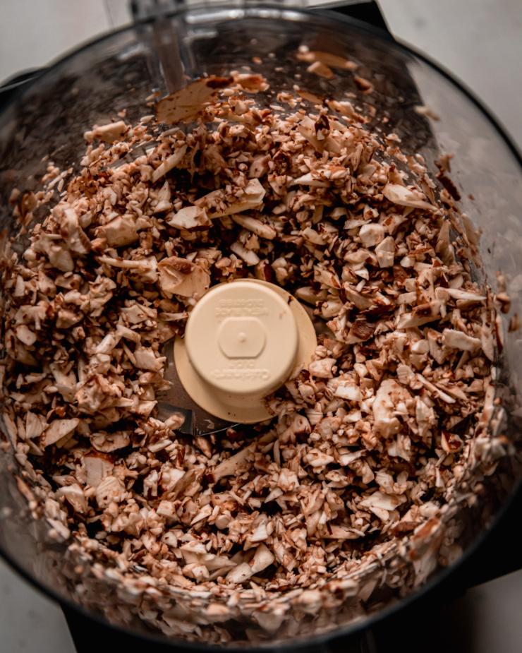 An overhead shot shows finely minced mushrooms in th ebowl of a food processor.