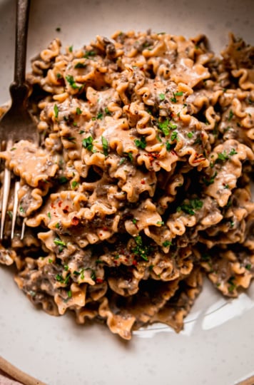 An overhead shot shows a bowl of creamy vegan pasta with a finely chopped mushroom and miso sauce. The pasta shape is like little ruffles and the whole dish is garnished with parsley.