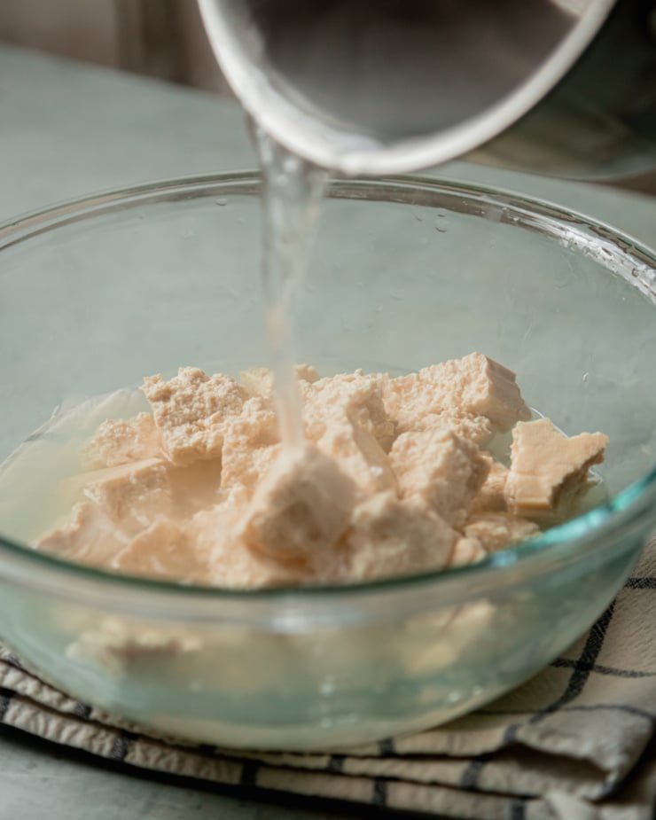 A head-on shot shows boiling salted water being poured over torn pieces of tofu in a bowl.