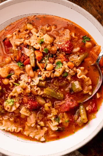 An up close, overhead shot shows a bowl of vegan minestrone soup with a spoon sticking out.