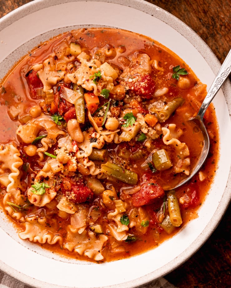 An up close, overhead shot shows a bowl of vegan minestrone soup with a spoon sticking out.