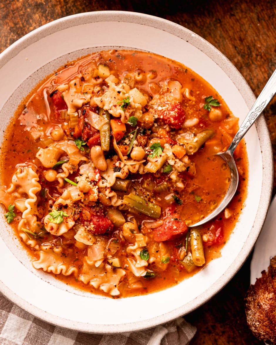 An overhead shot shows am individual bowl of vegan minestrone soup with a spoon sticking out.