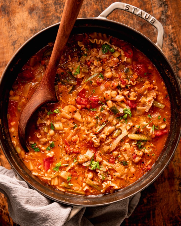 An overhead shot shows a pot of vegan minestrone soup. A wooden ladle is sticking out of the pot.