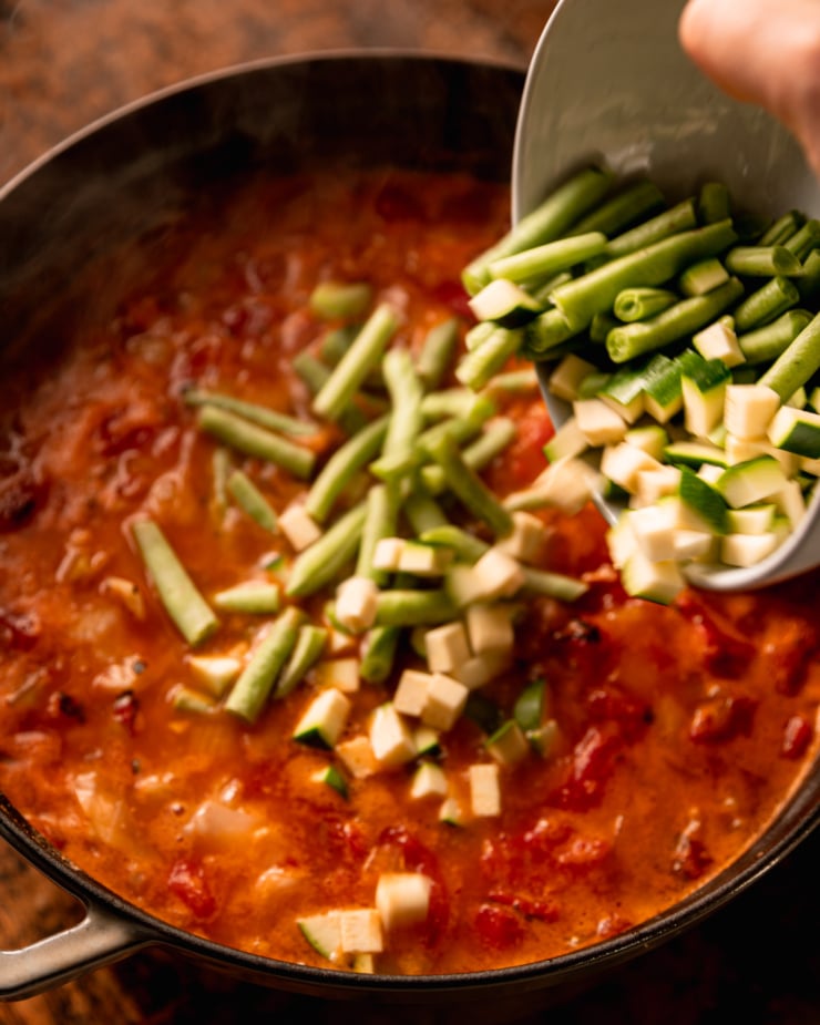 A slight 3/4 angle image shows cut green beans and diced zucchini being added to a pot.
