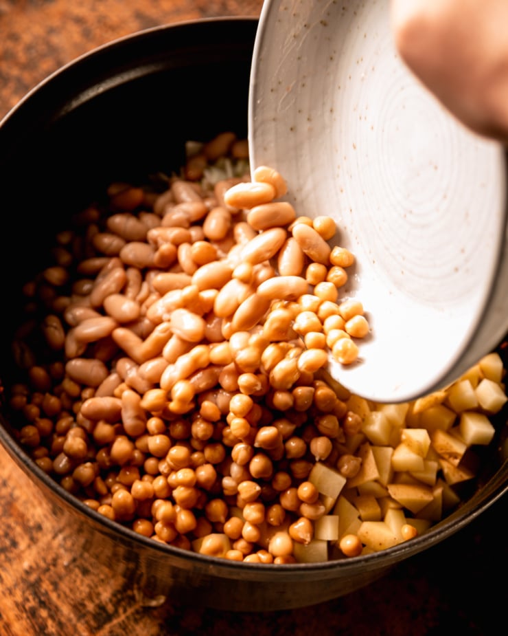 An overhead shot shows white kidney beans and chickpeas being added to a pot.