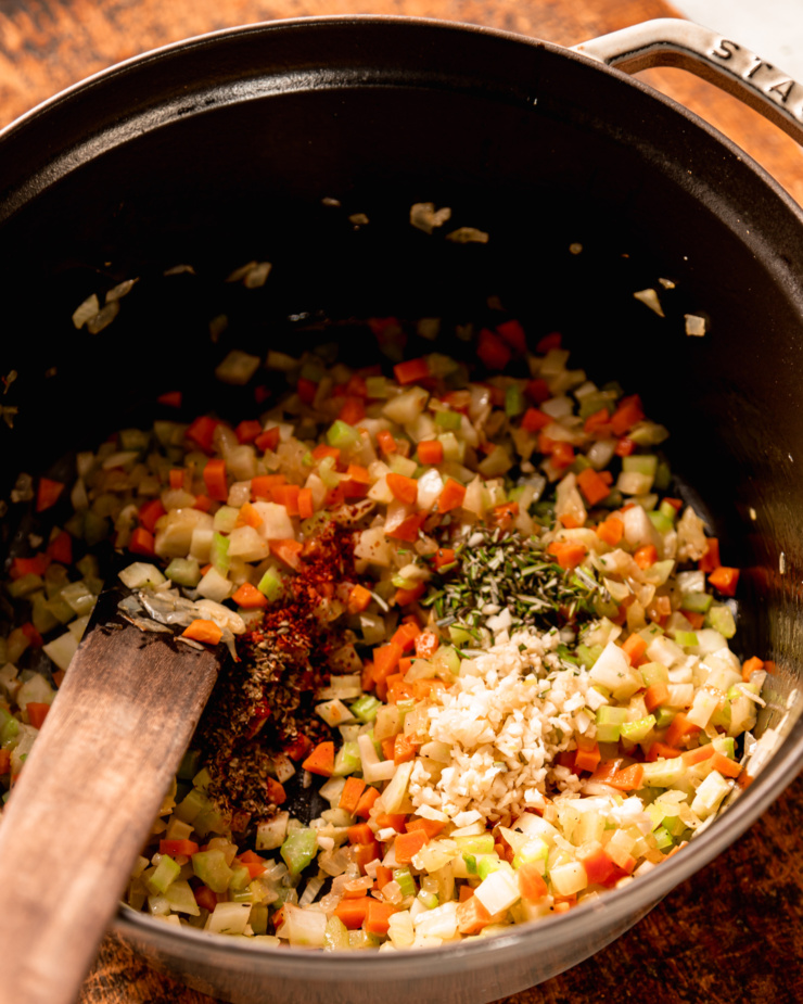 A 3/4 angle shot shows sautéed vegetables in a pot with chilies, minced garlic, dried oregano, and minced rosemary added.