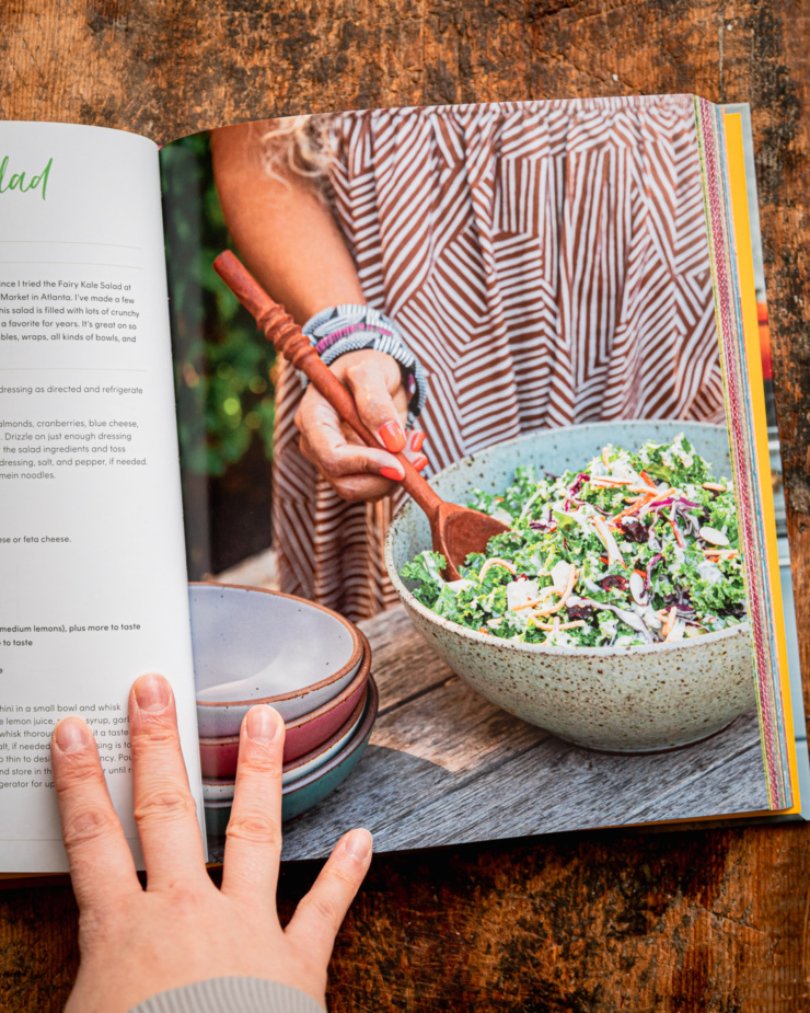 An overhead shot shows a photo of a crunchy kale salad with tahini dressing from inside the cookbook "Supper with Love" by Michelle Braxton.