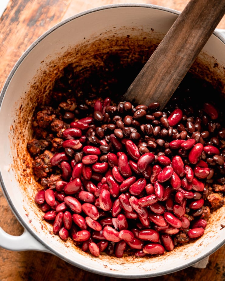 An overhead shot shows a Dutch oven filled with red kidney beans, black beans, and spices.