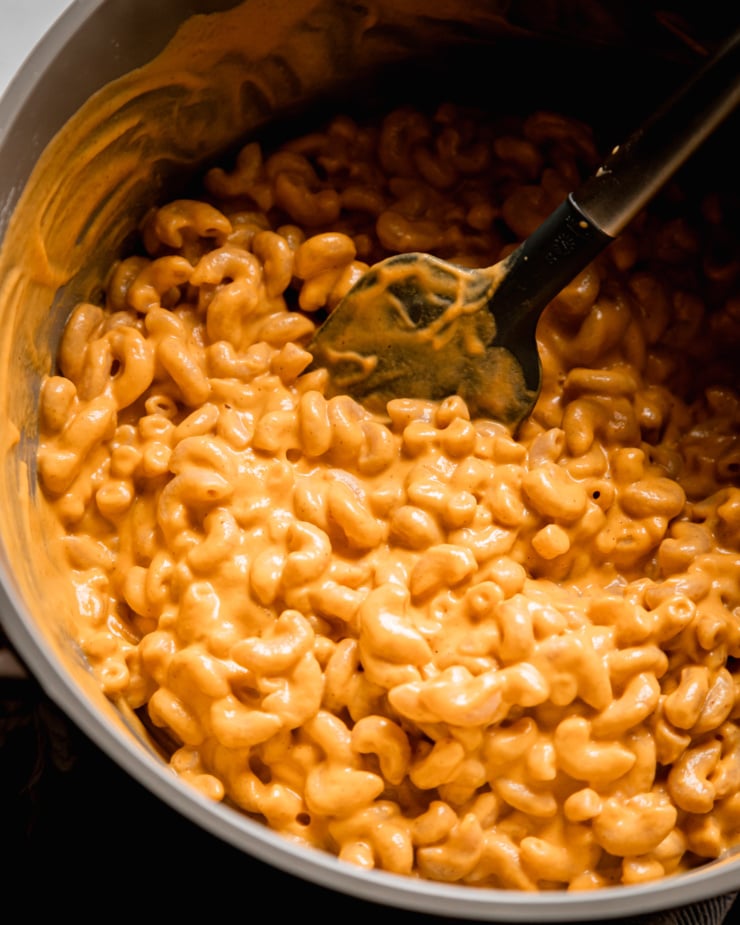 An overhead shot shows super creamy vegan truffle mac in a pot with a spatula. The sauce is light orange and looks incredible rich.