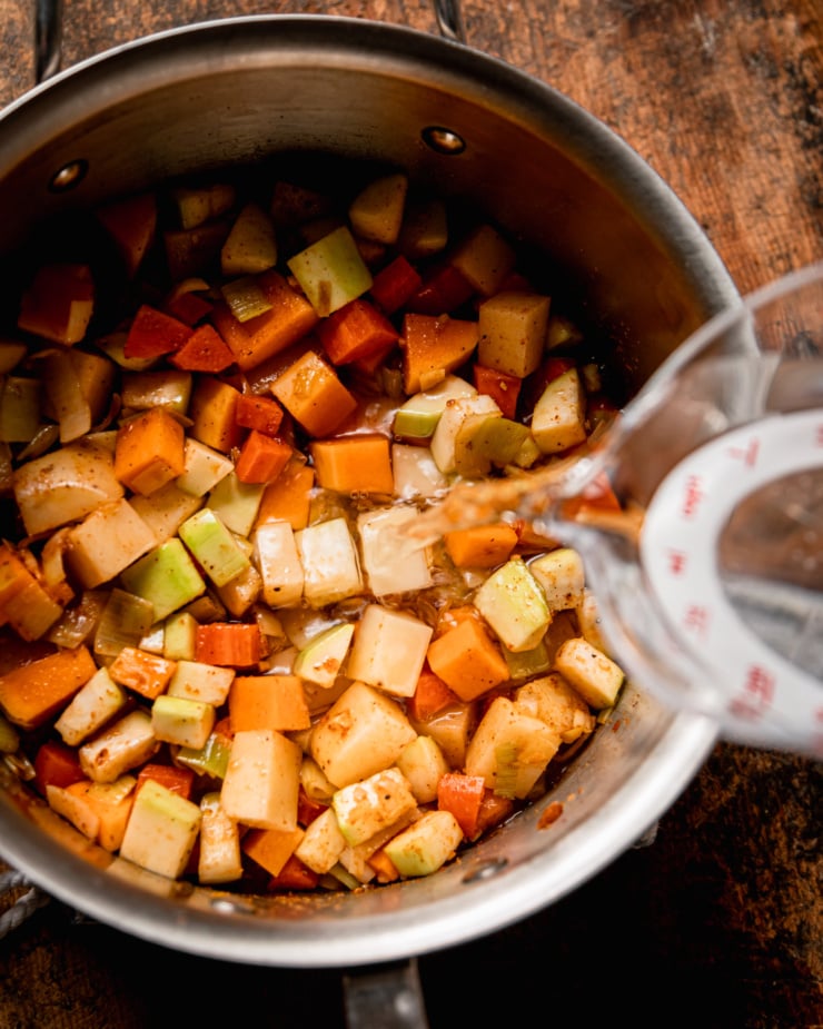 An overhead shot shows water being poured into a pot of diced vegetables.