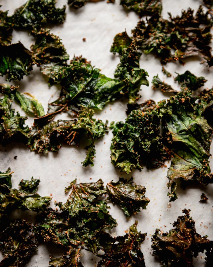 An overhead shot shows crispy baked kale pieces on a piece of parchment paper.