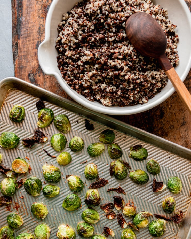 An overhead shot shows a large bowl with cooked quinoa and lentils all mixed together and a baking sheet with roasted halved brussels sprouts.