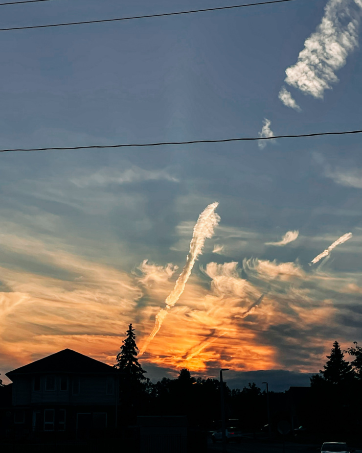 A head-on shot shows a sunset with lots of wispy clouds and shadows from a house and trees.