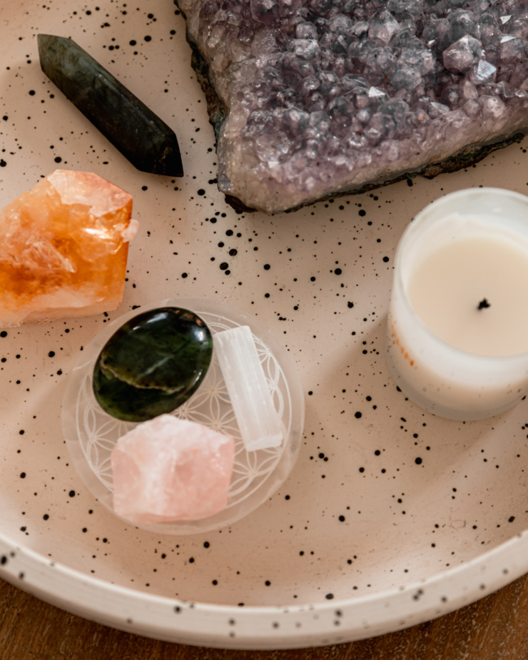 An up close, overhead shot shows some different crystals and a candle on a speckled ceramic tray.