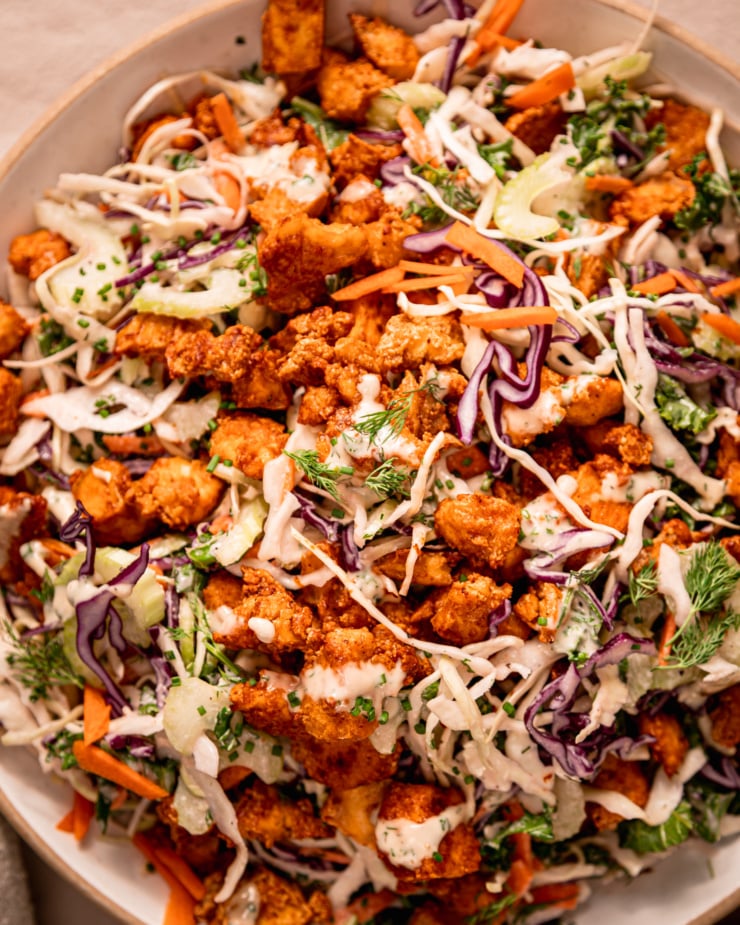 An up close, overhead shot shows a wide serving bowl filled with vegan ranch slaw and topped with crunchy baked Buffalo tofu pieces.