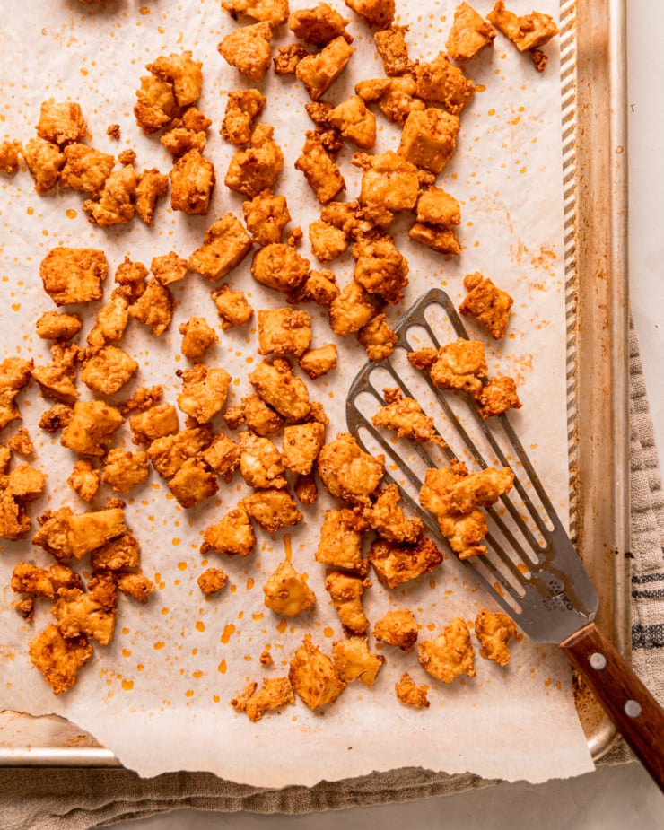 An overhead shot shows crispy baked tofu pieces on a baking sheet with a metal spatula nearby.